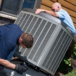 Two technicians in work attire installing an air conditioning unit for HVAC services by Cardinal Heating & Air Conditioning.