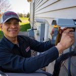 Technician in professional attire using tools on HVAC equipment outdoors for Cardinal Heating, Cooling, Plumbing & Electric.
