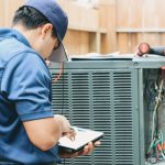 Technician using tablet to inspect air conditioning unit for Cardinal Heating, Cooling, Plumbing & Electric services.