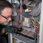 Technician repairing a furnace with complex wiring and tools for HVAC maintenance at Cardinal Heating & Cooling.