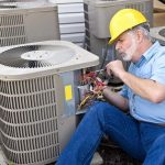 Technician in a yellow hard hat repairing air conditioning units for Cardinal HVAC services.