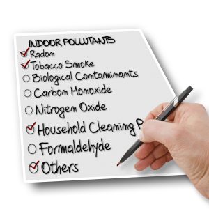 Hand holding a pen, checking off a list of indoor pollutants including radon, tobacco smoke, biological contaminants, carbon monoxide, nitrogen oxide, household cleaning products, formaldehyde, and others, emphasizing indoor air quality issues.