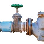 Industrial valve mechanism with a green handwheel and rusty metal, essential for plumbing in HVAC systems.