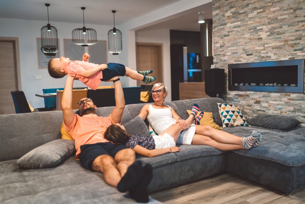 Family enjoying quality time on a comfortable sofa, with dad playfully lifting a young boy, while a girl relaxes beside them, illustrating home comfort and family connection during power outages.