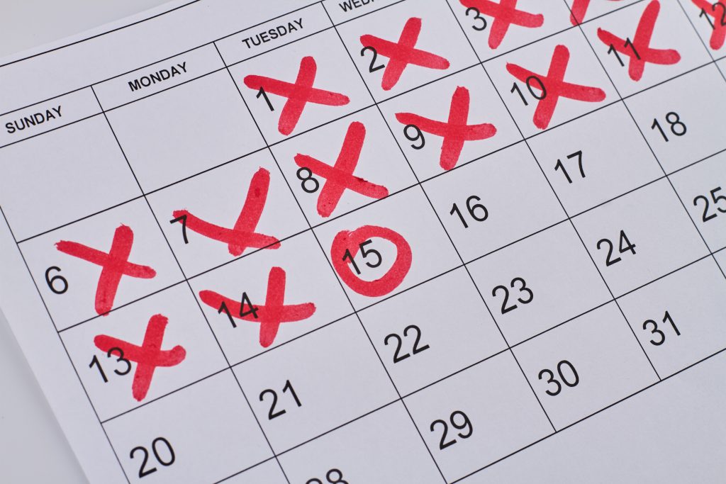 Paper calendar marked with red crosses and a circle on specific dates, symbolizing important maintenance reminders for HVAC systems.