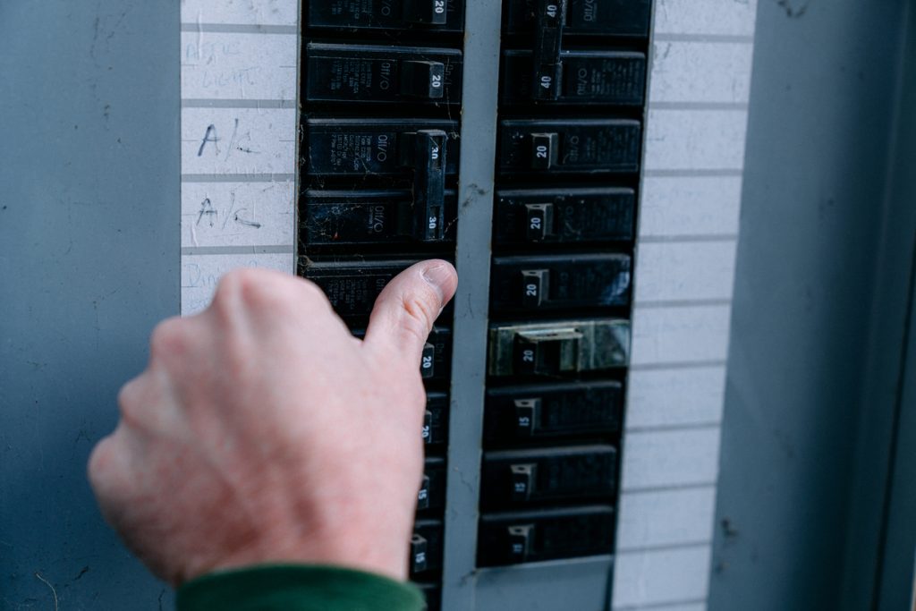 Hand flipping a circuit breaker in an electrical panel, highlighting potential overload issues during the holiday season.